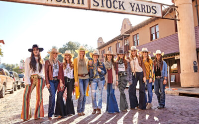 A group of women stand under the Fort Worth Stock Yards sign. They are decked head to toe in Western wear, and they are all wearing a fashion hat from American Hat Company.