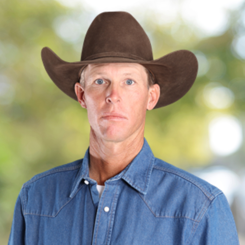 Bull rider Cooper James's headshot is shown. He's wearing a white button up shirt and a tan cowboy hat.